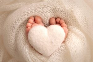 Soft feet of a new born in a white wool blanket Knitted white heart